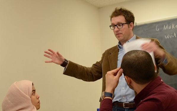 Joseph, our ESL Director is teaching his English 515 class. Two students are looking at him and paying attention to what he is saying. There is a black board behind Joseph.