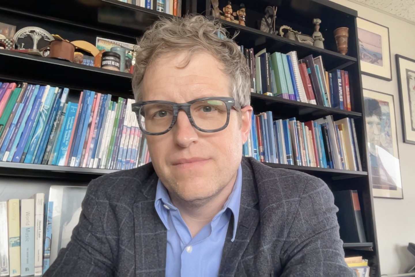 Headshot of Joseph Nosek, ESL Director. Joseph wears eyeglasses and sat in front of a bookcase. He wore a grey suit and a blue shirt.